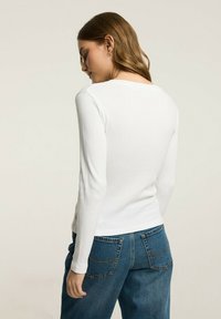Biała bluzka z długim rękawem o prążkowanej strukturze, z dekoltem w serek, w połączeniu z niebieskimi spodniami dżinsowymi z wysokim stanem z tylnymi kieszeniami.