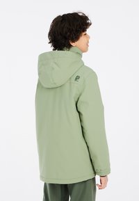 Giacca impermeabile verde con cappuccio, dotata di polsini elasticizzati e logo sulla parte superiore della schiena. Tessuto liscio, forma semi-adattata.