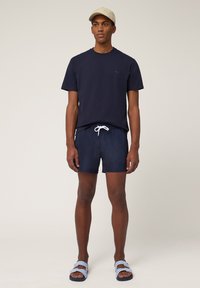 T-shirt navy, pantaloni da bagno con cordoncino e infradito a righe. Cappello khaki chiaro. Design semplice con colori solidi e stile casual.
