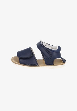 Sandalia de piel azul marino con tiras de velcro, diseño abierto, suela beige y detalles de costura blanca. Adecuada para el tiempo cálido.