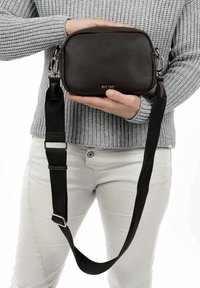 Braune Leder-Umhängetasche mit strukturierter Oberfläche, rechteckiger Form, Reißverschluss und einem verstellbaren schwarzen Schulterriemen. Akzentuiert mit silbernem Beschlag.