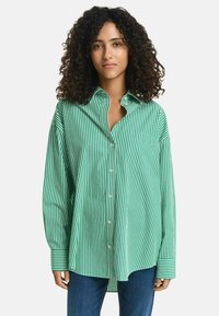 Camicia a righe verdi e bianche con una sola tasca sul petto, vestibilità comoda, maniche lunghe e colletto a risvolto, realizzata in tessuto leggero.