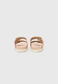 Nude slip-on sandaler med to justerbare stropper, en teksturert fotseng og en lysegrå gummisåle, sett bakfra.