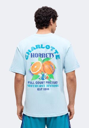 Mann trägt hellblaues T-Shirt mit Charlotte Hornets Basketball und orangem Design, Text über die Southeast Division und Full-Court-Press.