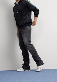 Felpa nera in velluto con strisce verdi, abbinata a jeans grigi sbiaditi con dettagli strappati e scarpe da ginnastica bianche con accenti.