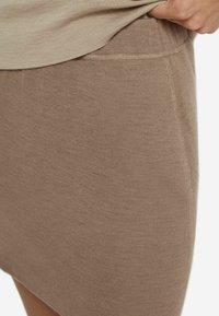 Bruine nauwsluitende rok gemaakt van gebreid materiaal. Heeft een zachte textuur met een platte tailleband en zichtbare naden.