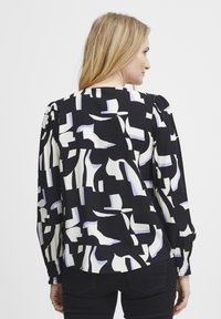 Blusa a maniche lunghe in tessuto nero con forme astratte bianche e lavanda, con polsini a sbuffo e scollatura rotonda.