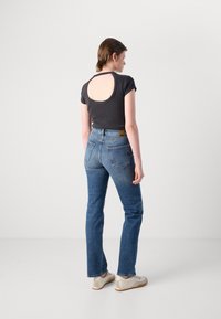 Grå kortermet skjorte med åpen rygg, kombinert med blå rette jeans. Hvite joggesko fullfører antrekket. Enkel og uformell design.