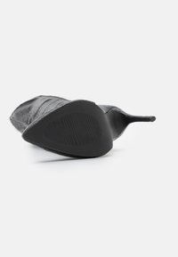 Chaussure à talons hauts noire avec un bout pointu et un dessus texturé. Semelle lisse avec un motif nervuré pour une meilleure adhérence. Design élégant et minimaliste.