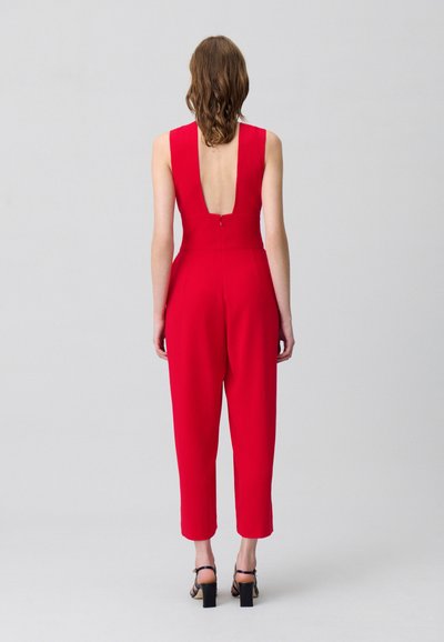 Mono rojo con un escote en V profundo, ajuste entallado, piernas cortas y una textura suave. Cierre en la parte posterior con una cremallera discreta.