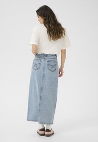 Svetlo modra denim dolga krila s prilegajočim pasom, vidno šivano in z dvema žepoma na hrbtu. V kombinaciji z majico v naravni barvi in obutvijo.
