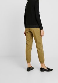 Zwarte trui met een gestructureerde zilveren accenten aan de zoom, gecombineerd met beige joggerbroeken en zwarte instappers met een zilveren detail.