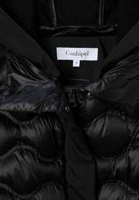 Doudoune noire avec un extérieur matelassé brillant et une doublure intérieure douce. Étiquette indiquant "Conbipel", taille "S". Fermeture éclair et éléments métalliques remarquables.