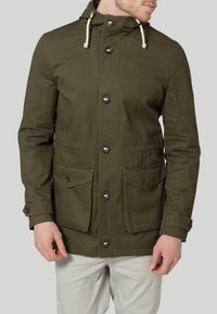 Veste en toile vert olive avec une capuche à cordon, des boutons sur le devant et deux poches sur la poitrine. Présente une finition texturée et des coutures visibles.