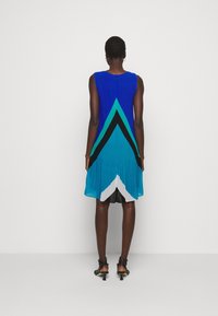 Robe sans manches avec un motif de blocs de couleur bleu, sarcelle et noir, une texture plissée et un ourlet incurvé. Le dos comporte une fermeture à boutons.