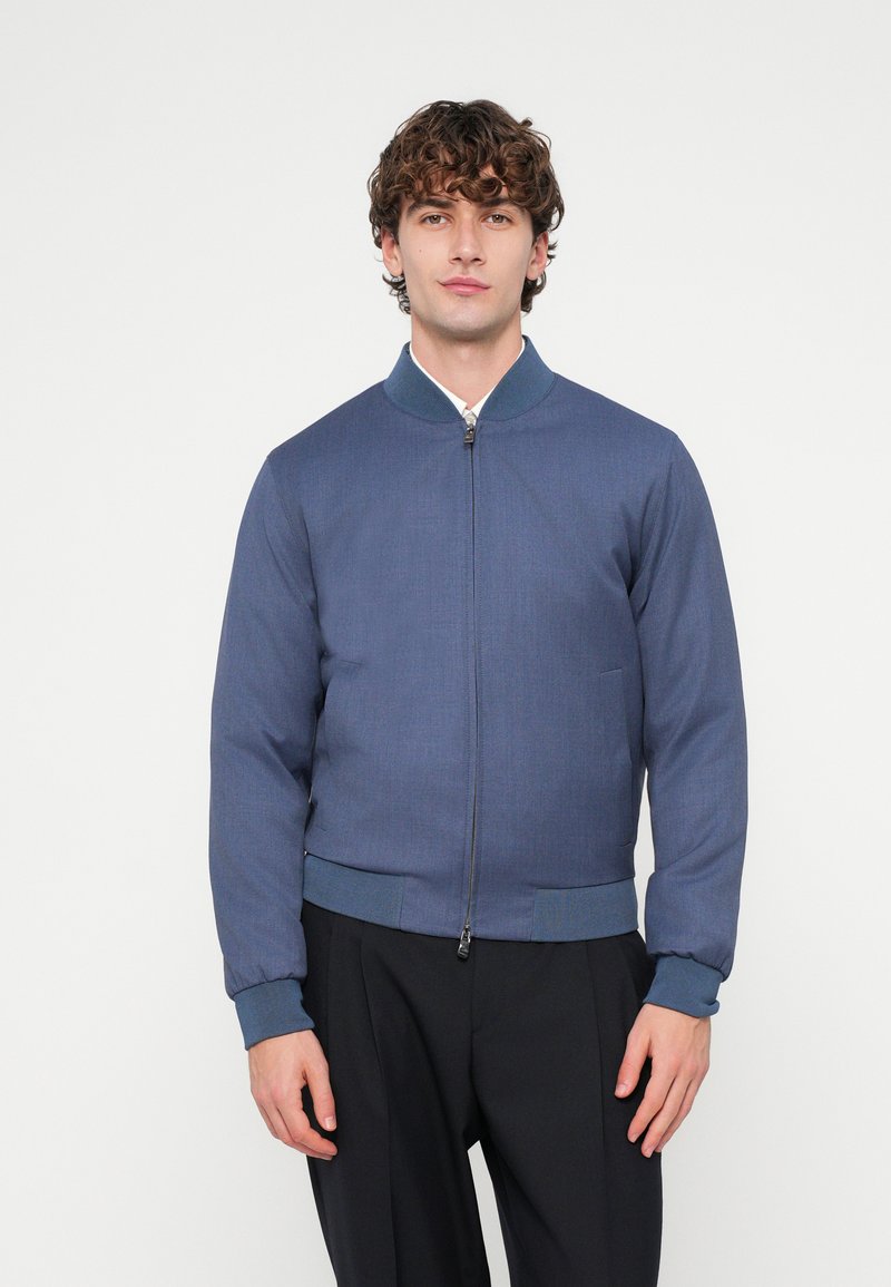 Blue bomber jacket made of textured fabric, featuring a zip front, ribbed collar and cuffs, and side pockets. Tailored fit.