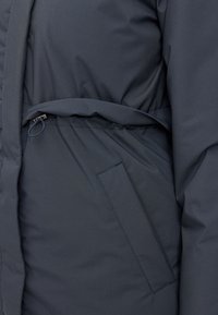 Navy blue puffer jacket with a belted waist, featuring a smooth, matte texture and a side pocket. Suitable for cold weather.