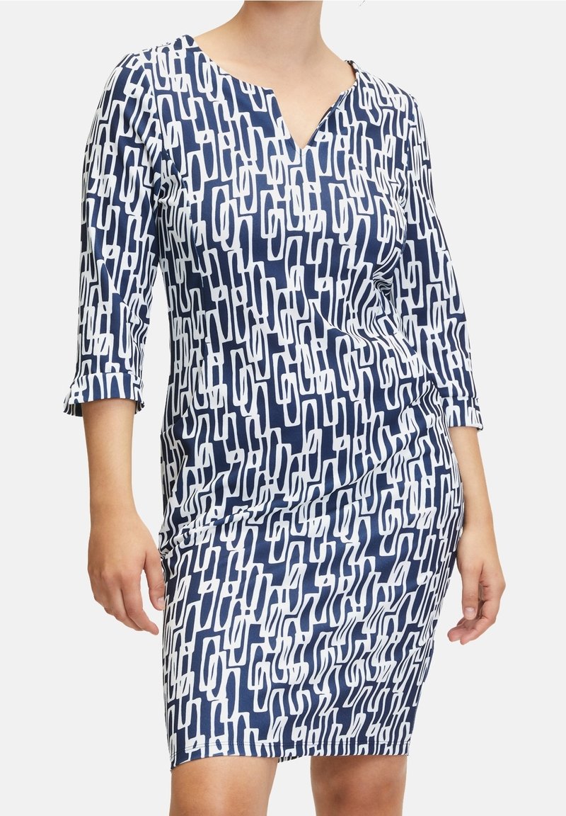 Femme portant une robe au genou avec des manches trois-quarts et un motif abstrait bleu marine et blanc de maillons de chaîne.