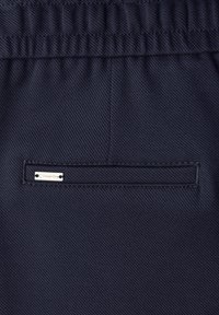 Marineblauer, strukturierter Stoff mit elastischem, gerafftem Bund. Verfügt über eine dekorative Gesäßtasche mit einem Metall-Logoanhänger und abgestepptem Rand.