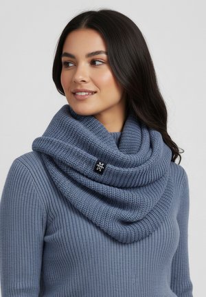 Woman wearing a blue ribbed sweater and knitted infinity scarf, looking to the side with loose dark hair and a slight smile.