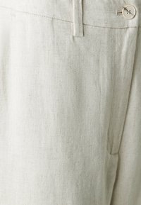 Pantalons en lin beige clair avec une texture lisse, présentant une fermeture à bouton et un détail de couture subtil. Design classique à coupe droite.