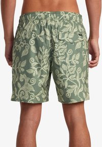 Pantaloni da bagno verdi realizzati in tessuto leggero, caratterizzati da un motivo a foglie bianche, vita elastica e una tasca posteriore con chiusura a bottone.