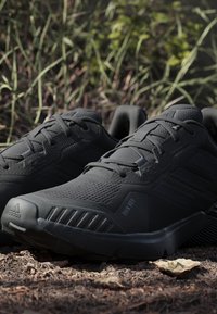 Chaussures de sport noires avec une tige en maille texturée, un col rembourré et une semelle extérieure en caoutchouc. Les caractéristiques incluent un design à lacets et des accents de marque.
