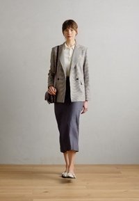Blazer z večbarvnimi črtami, bela bluzica, siva svinčnik krila in svetle balerinke. Srednje dolgi lasje, drži majhno torbico.