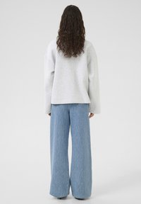 Lys grå oversized sweatshirt med brede ærmer, parret med højtaljede, flared, lyseblå denim jeans med en subtil tekstur.