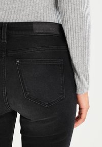 Vaqueros negros de corte ajustado, con una cintura alta, costuras tonales y un parche en la parte de atrás. La tela tiene una textura suave y ligeramente desgastada.