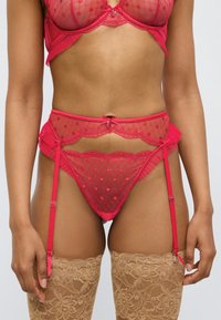 Σετ κόκκινου διάφανου εσώρουχου με δίχτυ με σχέδιο καρδιές και βολάν στις άκρες, με ζαρτιέρα και διακοσμητικές μεταλλικές λεπτομέρειες.