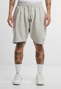 Lys grå bomullsshorts med elastisk midje, sidelommer og rå kanting, kombinert med hvite sneakers og ankelsokker.