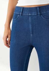 Tumedat sinised denim teksad kõrge vöökohtaga, millel on viis taskut, vöökohaga aasad ja peen kulumine reite piirkonnas.