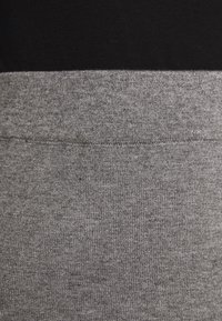 Gros plan d'une ceinture en tissu tricot gris avec détail de couture sur fond noir.