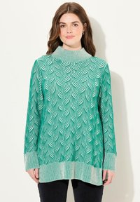 Pull en tricot vert avec un col montant, présentant un motif en vagues et des poignets rayés. Le tissu est doux avec une finition texturée.