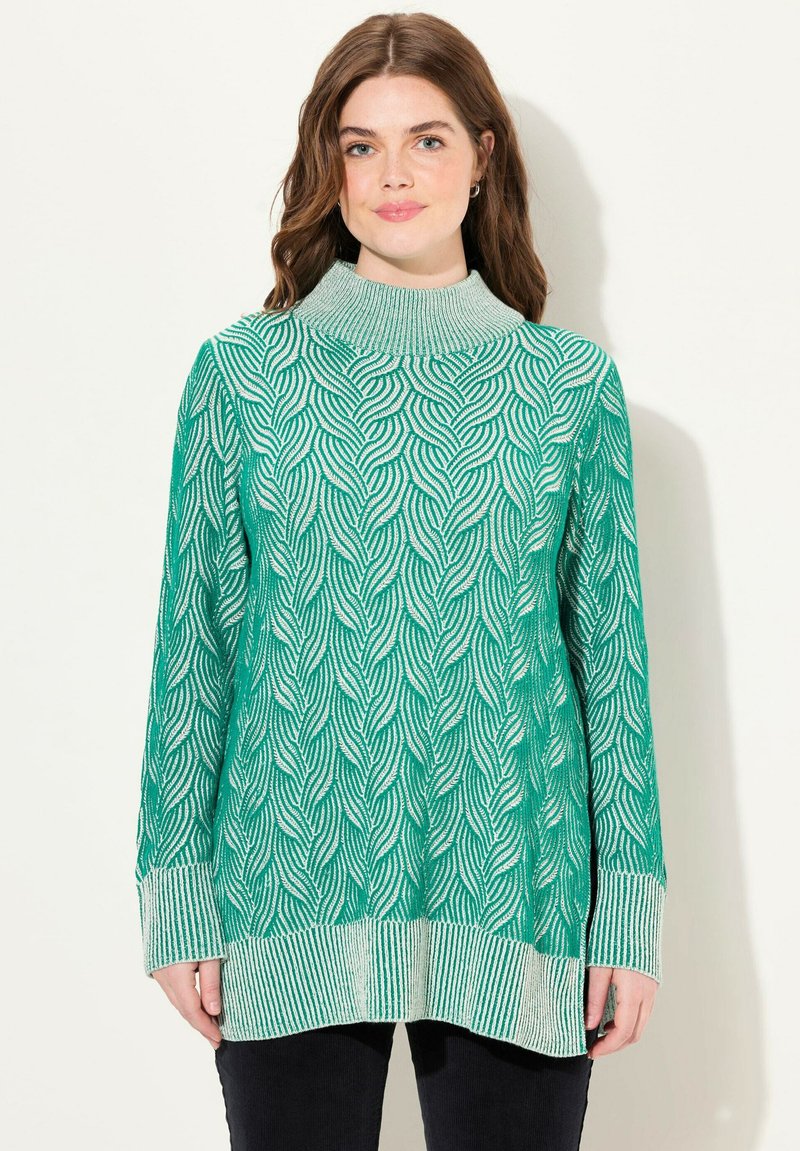 Pull en tricot vert avec un col montant, présentant un motif en vagues et des poignets rayés. Le tissu est doux avec une finition textur�ée.