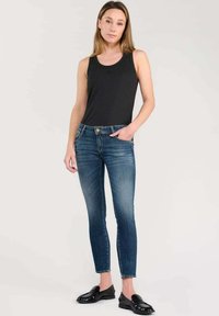 Top negro sin mangas, jeans ajustados azules con ligero desgaste, de longitud hasta los tobillos, combinados con mocasines negros brillantes. Diseño sencillo sin patrones visibles.