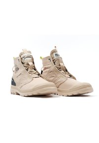 Beżowe buty za kostkę z teksturowanej tkaniny, gumową podeszwą i czarnymi akcentami, wyposażone w szybki system sznurowania i metki z logo.