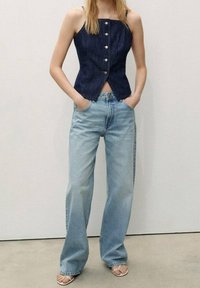 Denim-mallinen korsettitoppi, jossa hopeiset napit ja säädettävät olkaimet, yhdistetty vaaleansinisisiin leveälahkeisiin farkkuihin ja valkoisiin remmikenkiin.