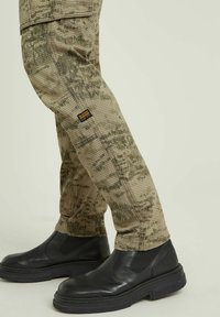 Beige mönstrade cargo-byxor med rutigt tryck, utrustade med en sidoficka och parades med svarta läderankelboots.