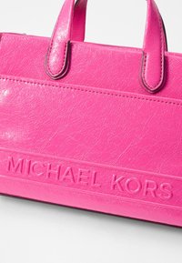 Borsa sintetica rosa con superficie testurizzata, due manici arrotondati e logo "MICHAEL KORS" in rilievo sul davanti.