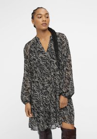 Abito nero e beige a fantasia realizzato in tessuto leggero, con scollatura a V, maniche lunghe e design a strati, dalla vestibilità ampia.