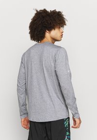 Camiseta de manga larga gris hecha de tela suave, con cuello redondo y corte relajado. Detalle de costura sutil en la parte posterior.