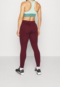 Sportovní outfit zahrnující sportovní podprsenku s řidším zaobleným zadním dílem v mentolově zelené barvě a přiléhavé legíny barvy burgundské, doplněný černými sportovními botami a bílými ponožkami.