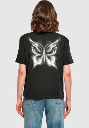 Black cotton t-shirt featuring a large white butterfly graphic on the back. Short sleeves and a relaxed fit, with blue denim jeans.