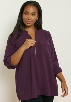 Maglione bordeaux a maglia con scollatura a V e chiusura a mezza zip, dotato di due tasche sul petto e maniche arrotolate per un fit rilassato.