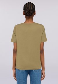 Khakifarbenes Baumwoll-T-Shirt mit kurzen Ärmeln, geradem Schnitt, Rundhalsausschnitt und glattem Material, kombiniert mit hellblauen, hochgeschnittenen Jeans.