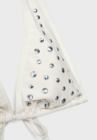 Haut de bikini blanc avec des clous ronds argentés disposés en motif dispersé, doté de liens réglables en bas.