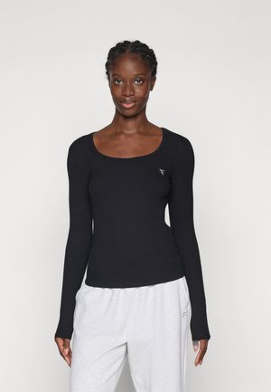 Black ribbed long-sleeve top with a scoop neckline and a small triangular logo accent on the chest, paired with grey sweatpants.