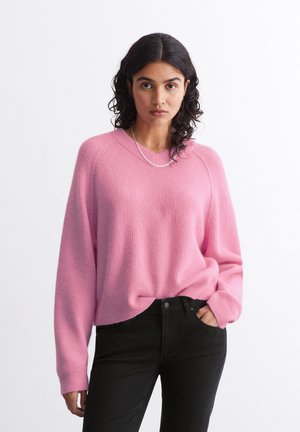 Pink knit sweater with a relaxed fit, ribbed texture, and crew neckline, paired with black jeans. Simple silver chain necklace accent.